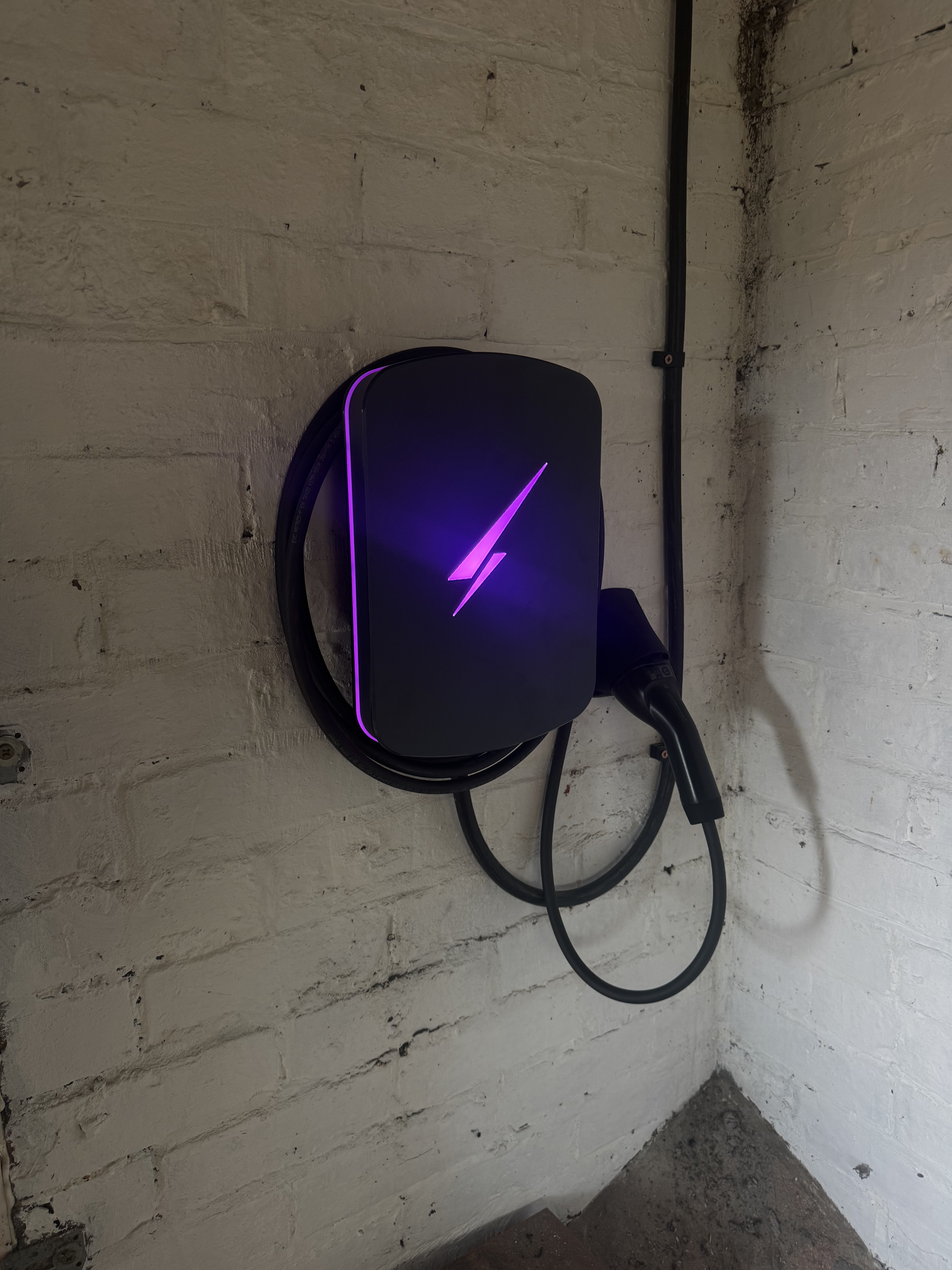 Black Hypervolt EV charger glowing purple, installed on a white painted brick wall with the cable neatly coiled