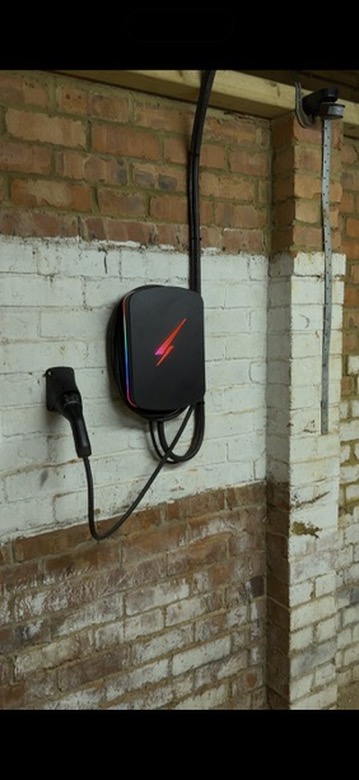 Black Hypervolt EV charger with a red glowing edge installed on a whitewashed garage wall