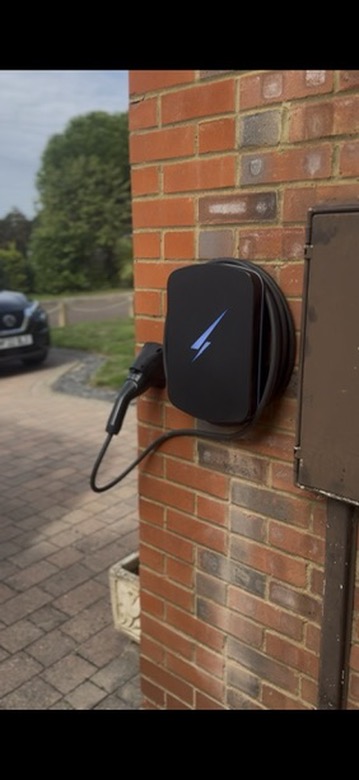 Black Hypervolt EV charger installed on the red brick corner of a driveway, with a car charging